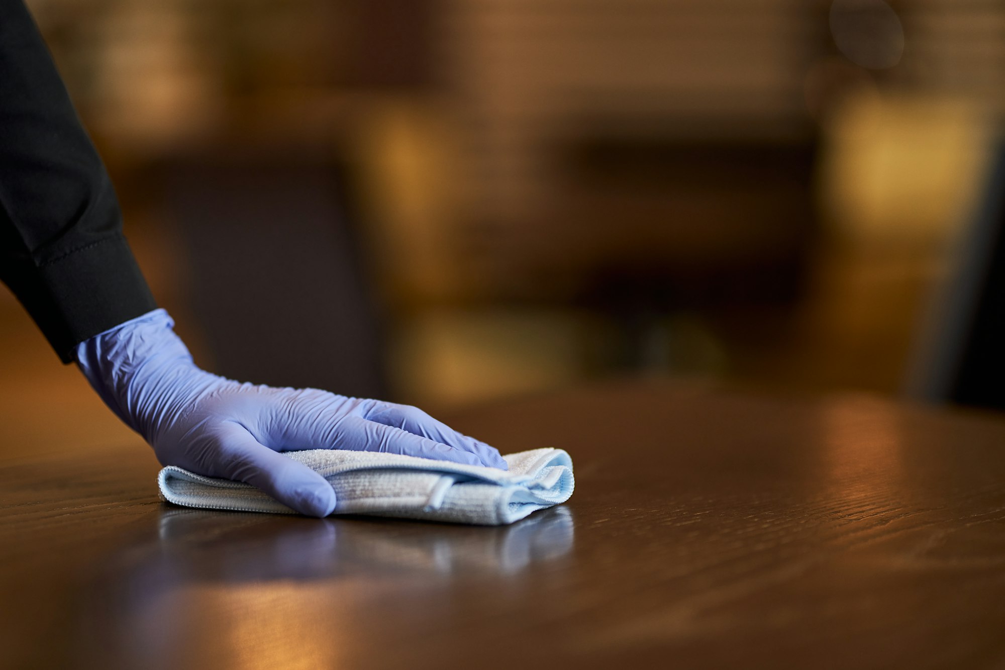 Person with gloves on cleaning and sanitizing a wooden table